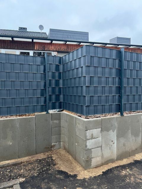 Über Eck geführter Doppelstabmattenzaun mit Sichtschutzstreifen auf einer Mauer aus Betonsteinen