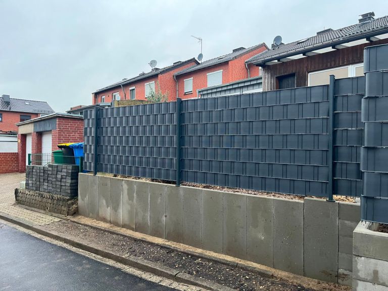 Lange Zaunanlage mit Sichtschutz entlang einer Wohnstraße, auf einer neuen Mauer montiert